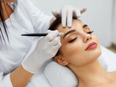 Permanent Makeup For Eyebrows. Closeup Of Beautiful Woman With Thick Brows In Beauty Salon. Beautician Doing Eyebrow Tattooing For Female Face. Beauty Procedure. High Resolution